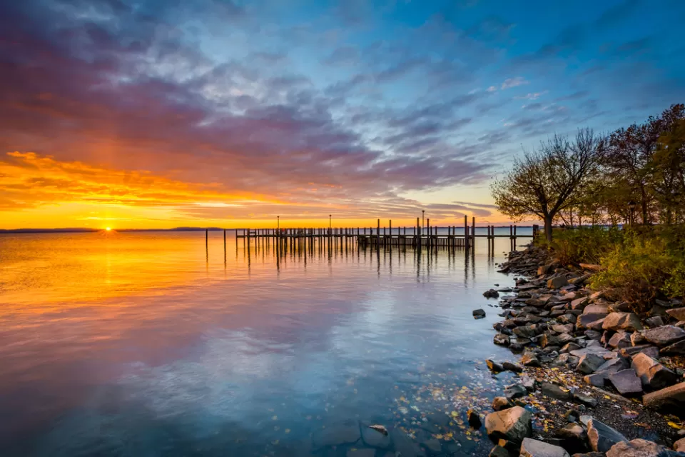 Colorful sunset viewed from rockly shoreline on Chesapeake Bay with dock in distance